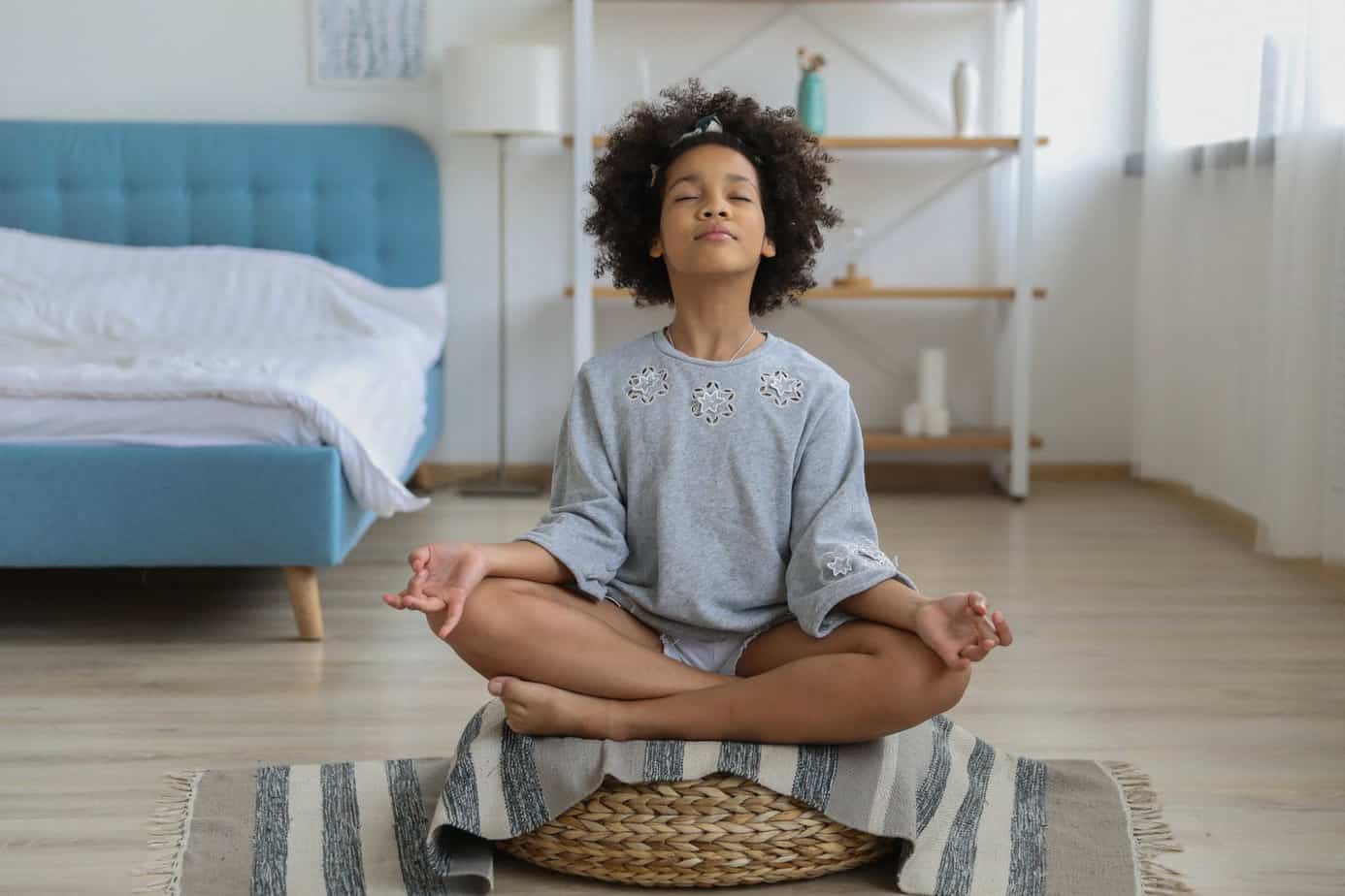 girl meditating in room on a meditation cushion with eyes closed thinking about om