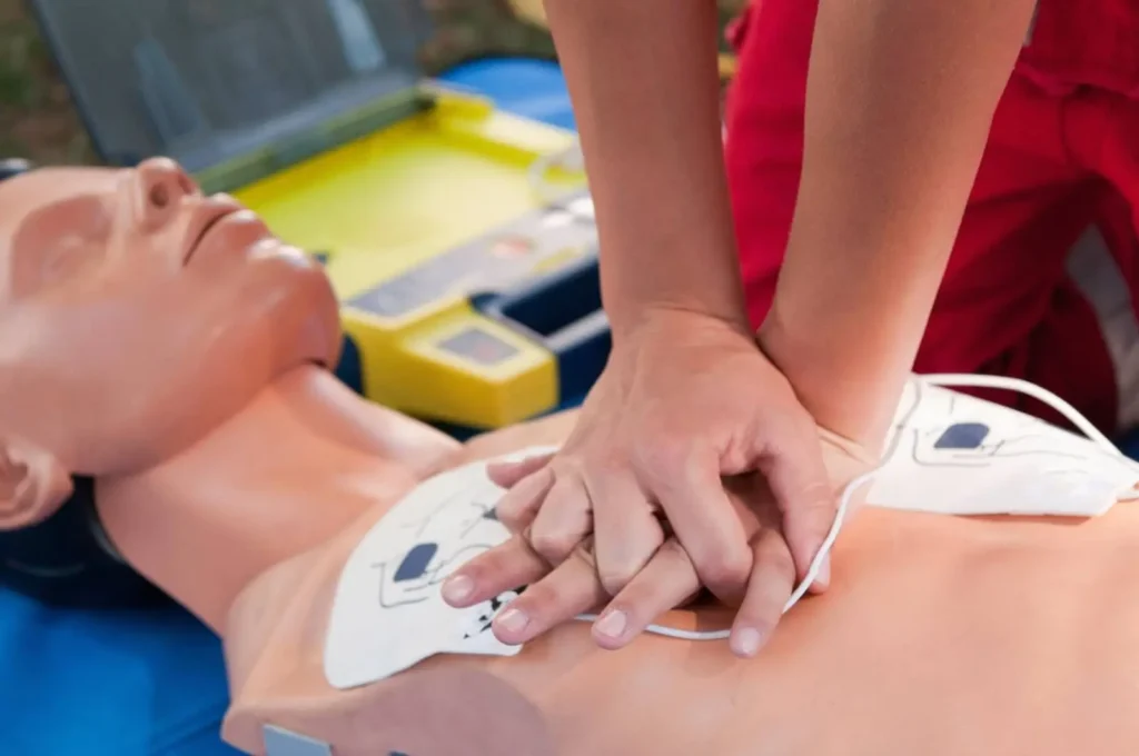 A CPR demonstration on a dummy. Two hands are pressing down on the dummy's chest.