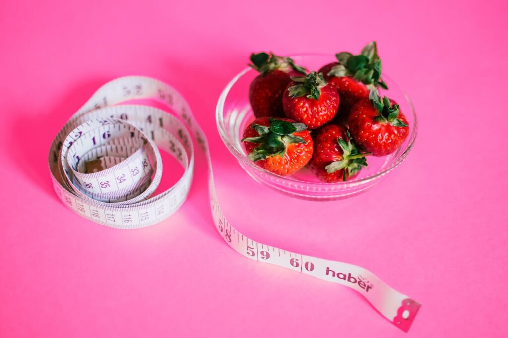 A rolled up tailors tape measure next to a small bowl of strawberries