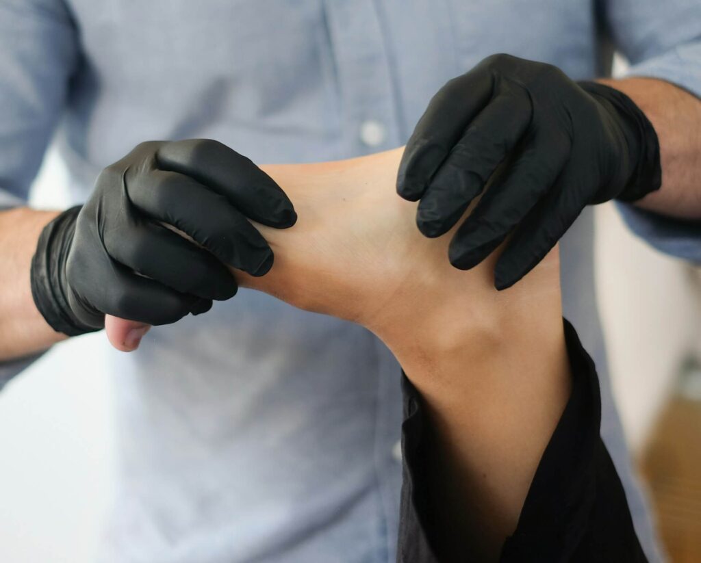 A person wearing black latex gloves massages another person's foot
