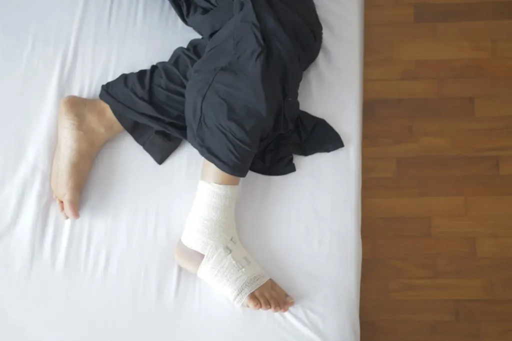 A person lays down on a bed and their right foot is bandaged