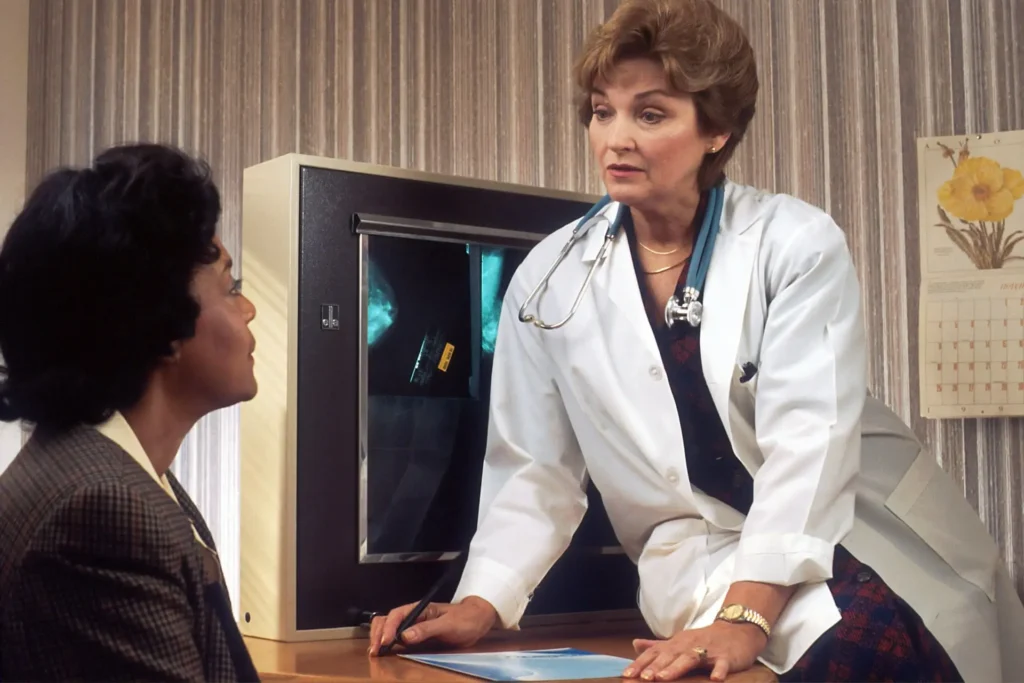 A female doctor sits on a desk and is consulting her patient.
