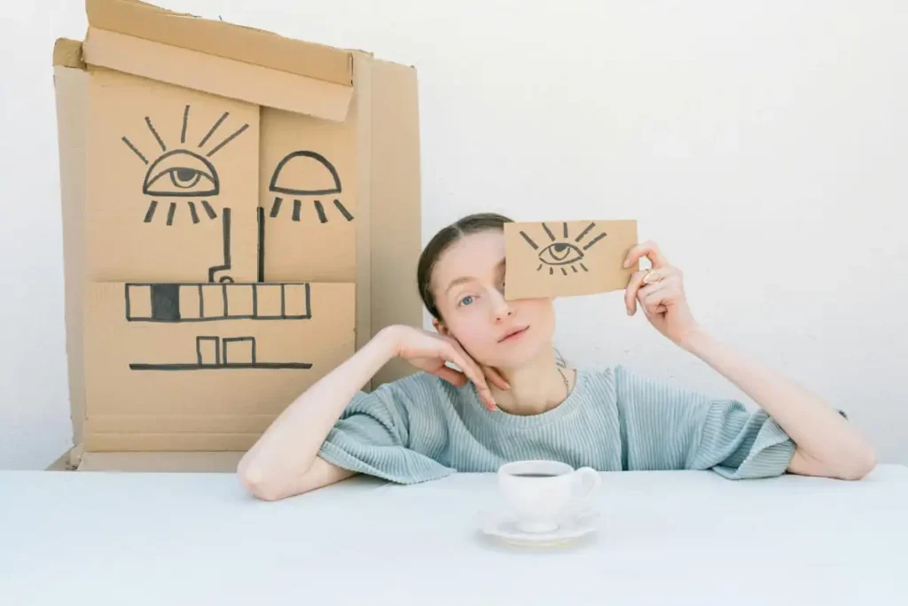 A woman sits with a piece of cardboard covering one eye. The piece of cardboard has a drawing of an eye on it.