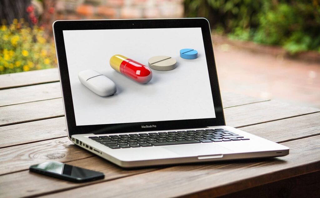 A laptop is open and sits on a table. On the laptop screen several pills are shown