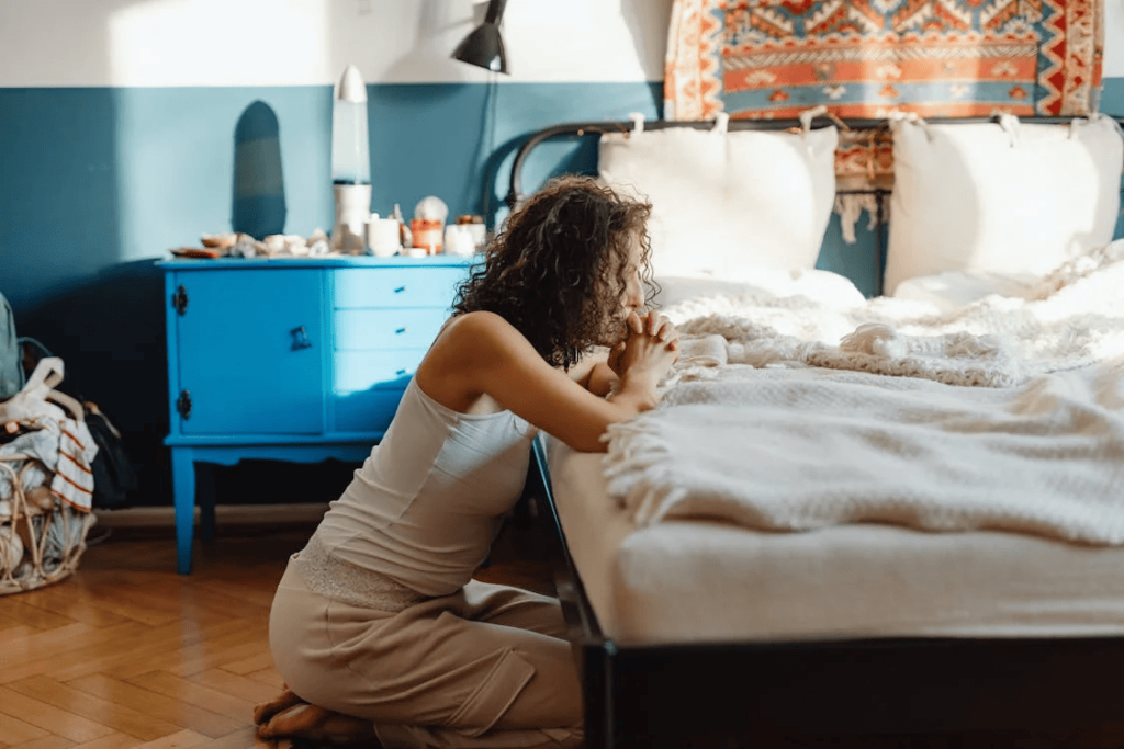 a woman kneels at a bedside and prays