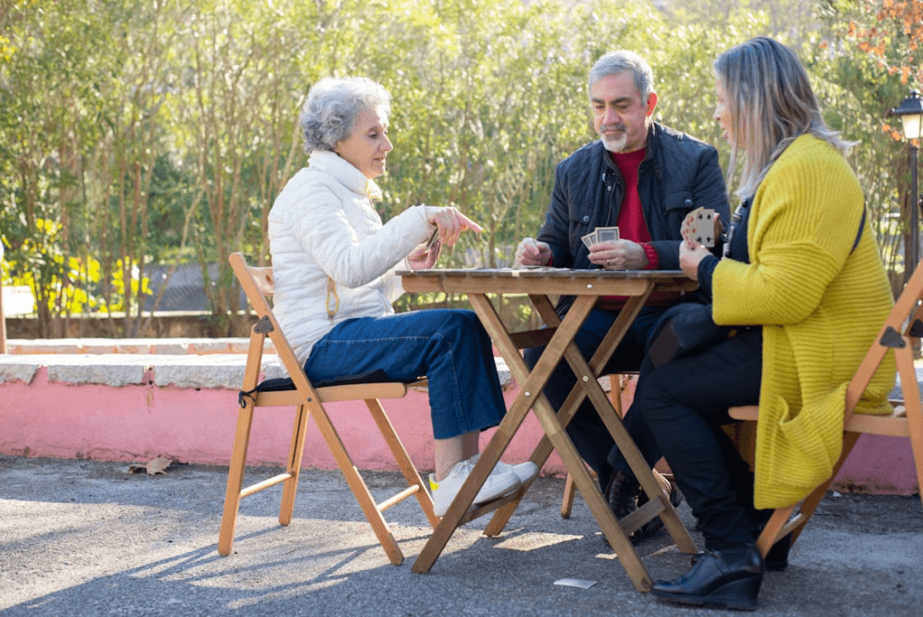 Three people sit at a table playing a card game.